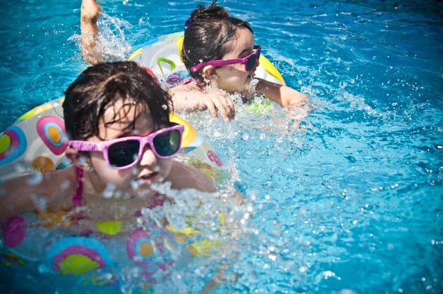 two children swimming in a pool with goggles and floaties in the summer sun